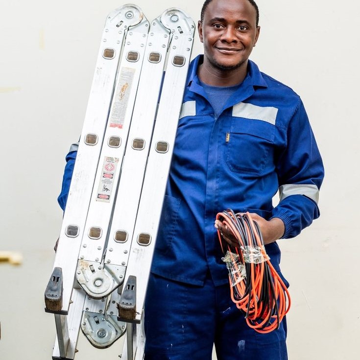 a man dressed in a blue electrcal engineering vest holding a ladder and an electrical wire 